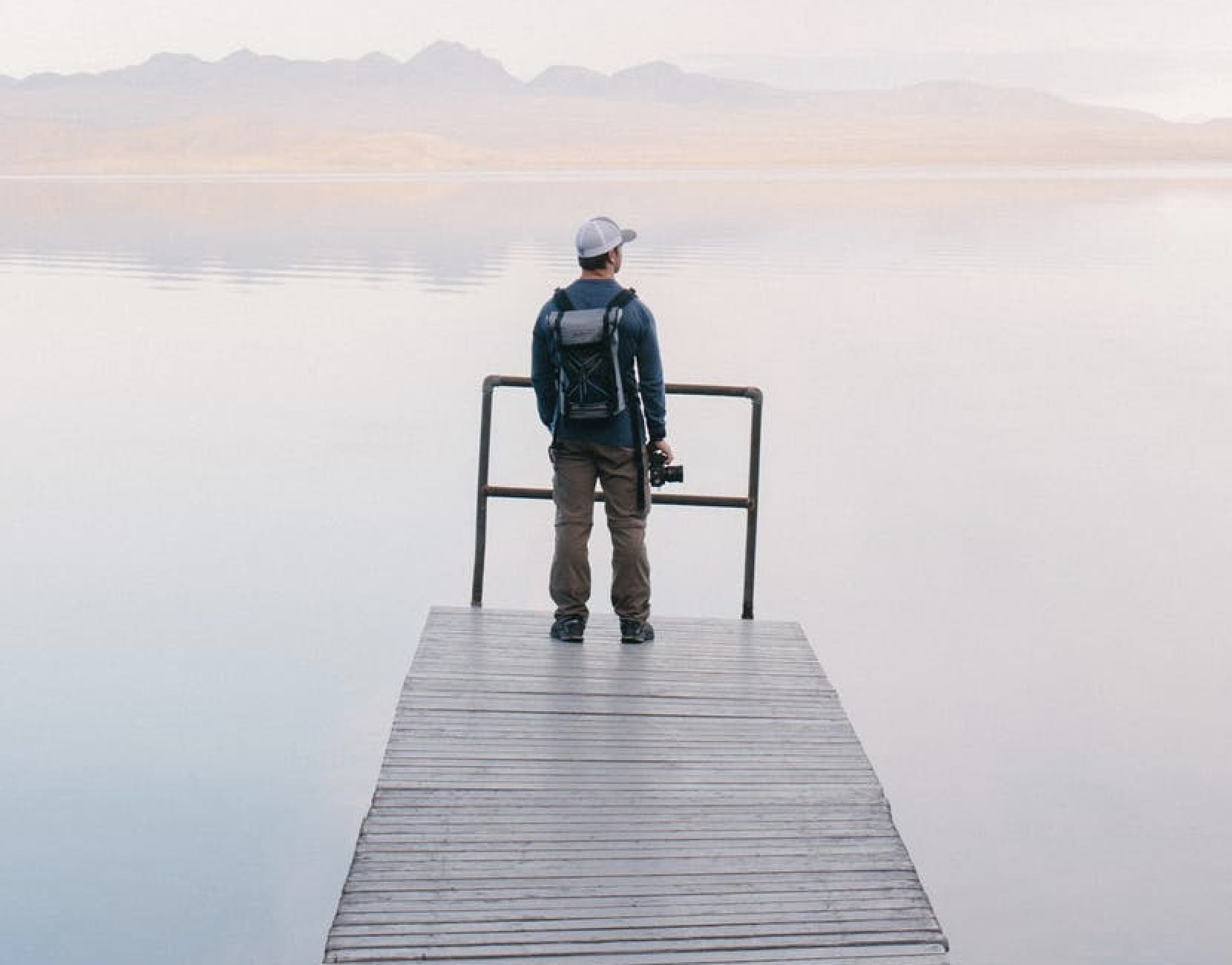 man standing on a peer overlooking a lake